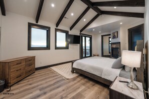 A bedroom with a large bed, wooden dresser, and a stone fireplace.