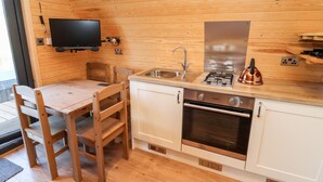 A compact kitchen with wooden walls, a built-in stove, a sink, and a flat-screen TV mounted on the wall. - Gander Pod (Worcester)