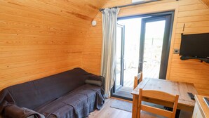 A cozy room with a wooden floor, a sofa, a table, and a TV mounted on the wall. - Gander Pod (Worcester)