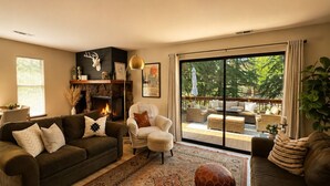 A living room with a fireplace, a sofa, a chair, and a large sliding glass door leading to an outdoor patio.