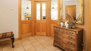 A corner room with wooden doors, a bench, a dresser, and a mirror. - Stable Cottage (Inverurie)