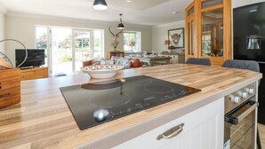 A modern kitchen with a large island, built-in oven, and a dining area with a view to the outdoors. - Stable Cottage (Inverurie)