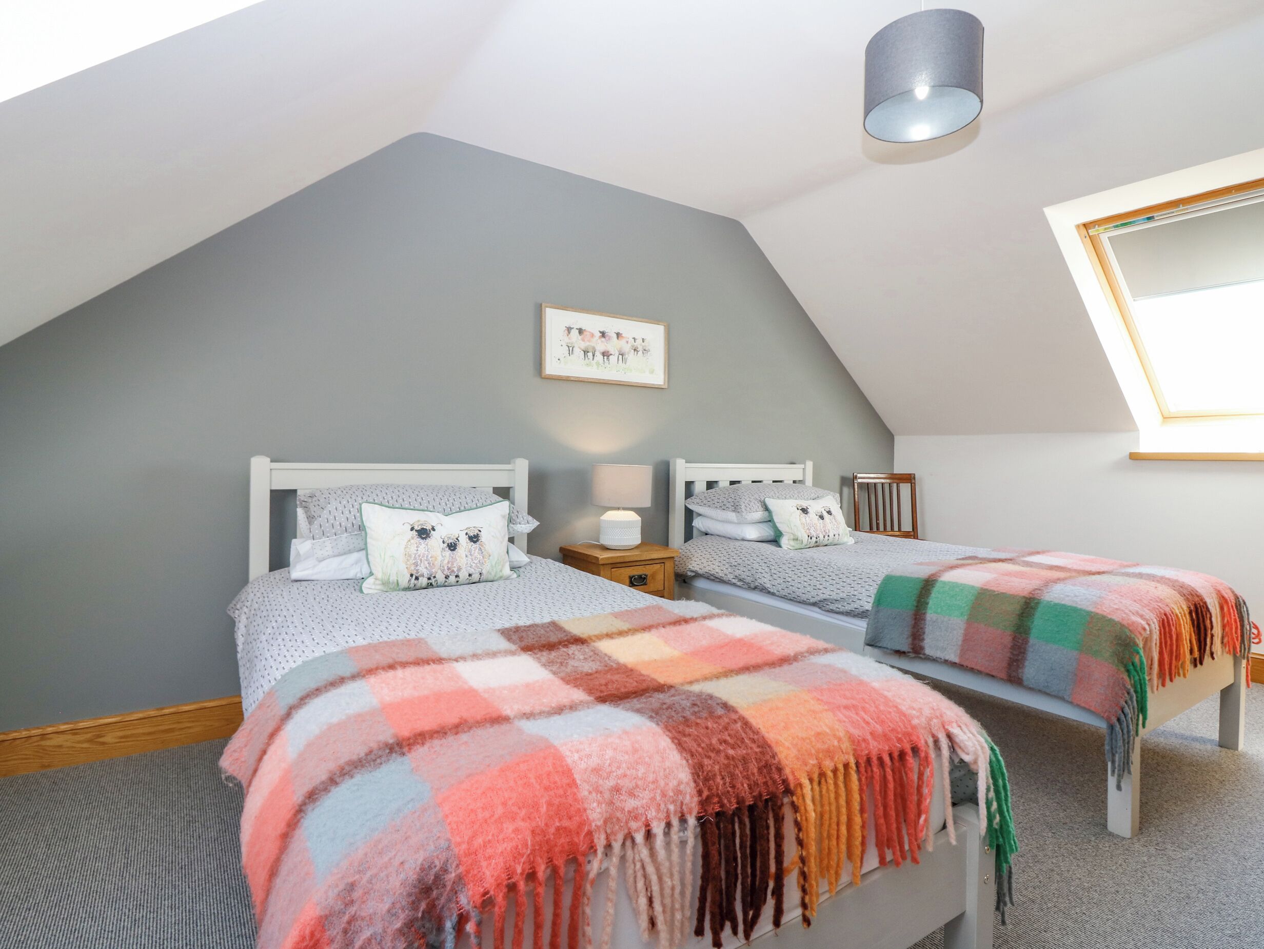 A bedroom with two beds, a skylight, a bedside lamp, and a framed picture on the wall.