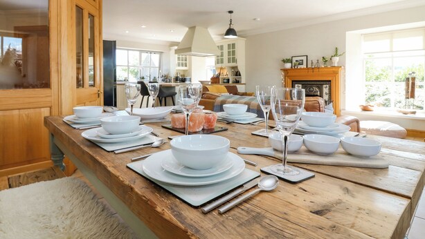 A dining area with a wooden table set for a meal, a kitchen in the background, and a fireplace. - Stable Cottage (Inverurie)