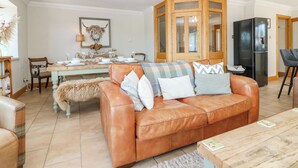 A living room with a brown leather sofa, a wooden dining table set for four, a black refrigerator, and a wooden cabinet with glass doors. - Stable Cottage (Inverurie)