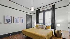 Un dormitorio con cama, mesita de noche, lámpara y cuadros en la pared.