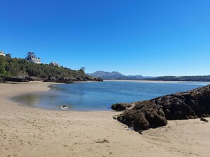 A beach with clear blue water, sandy shore, and rocky outcrops. - Bryn Derfel (Porthmadog)