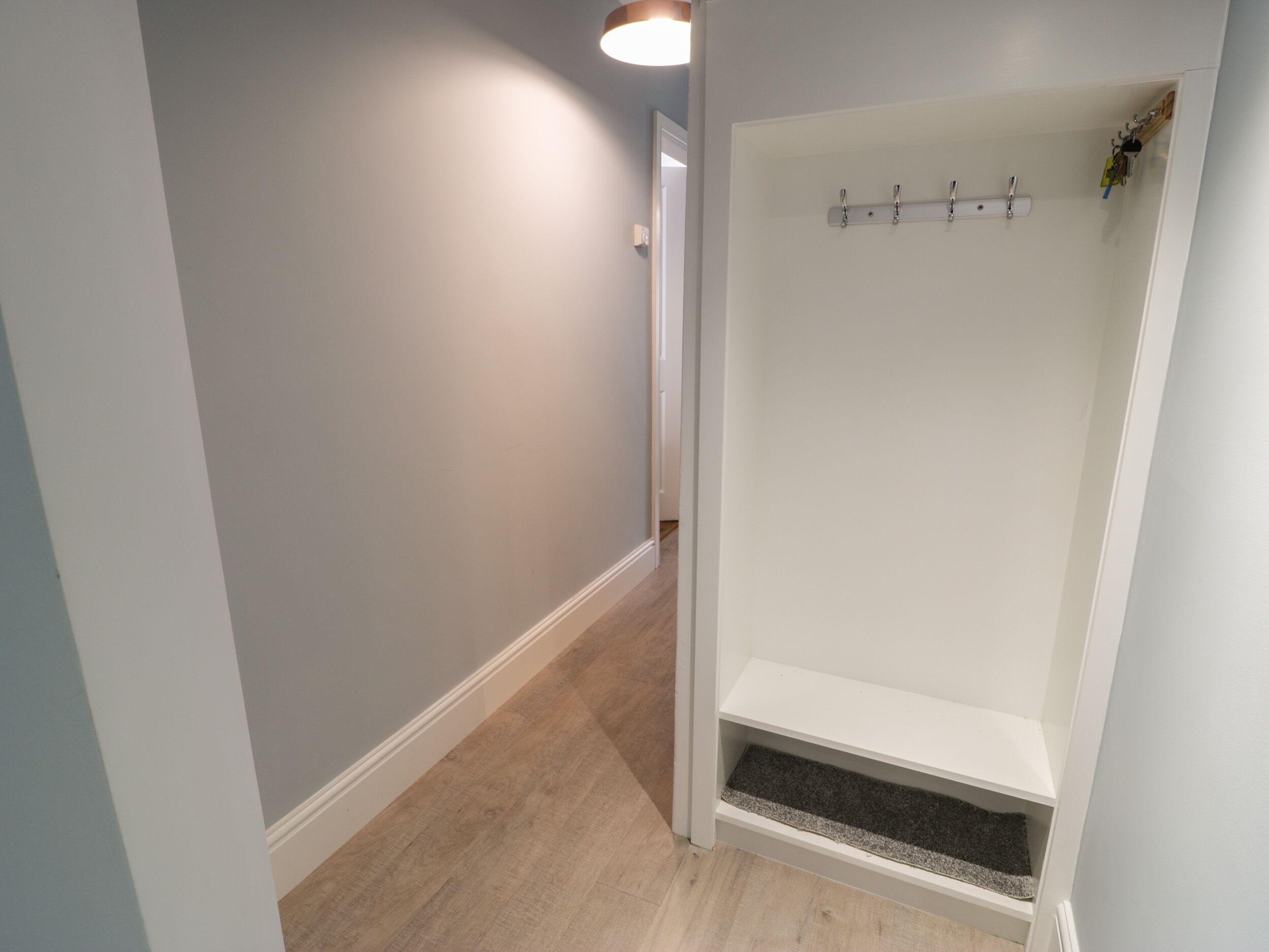 Een hal met een houten vloer en een witte muur.