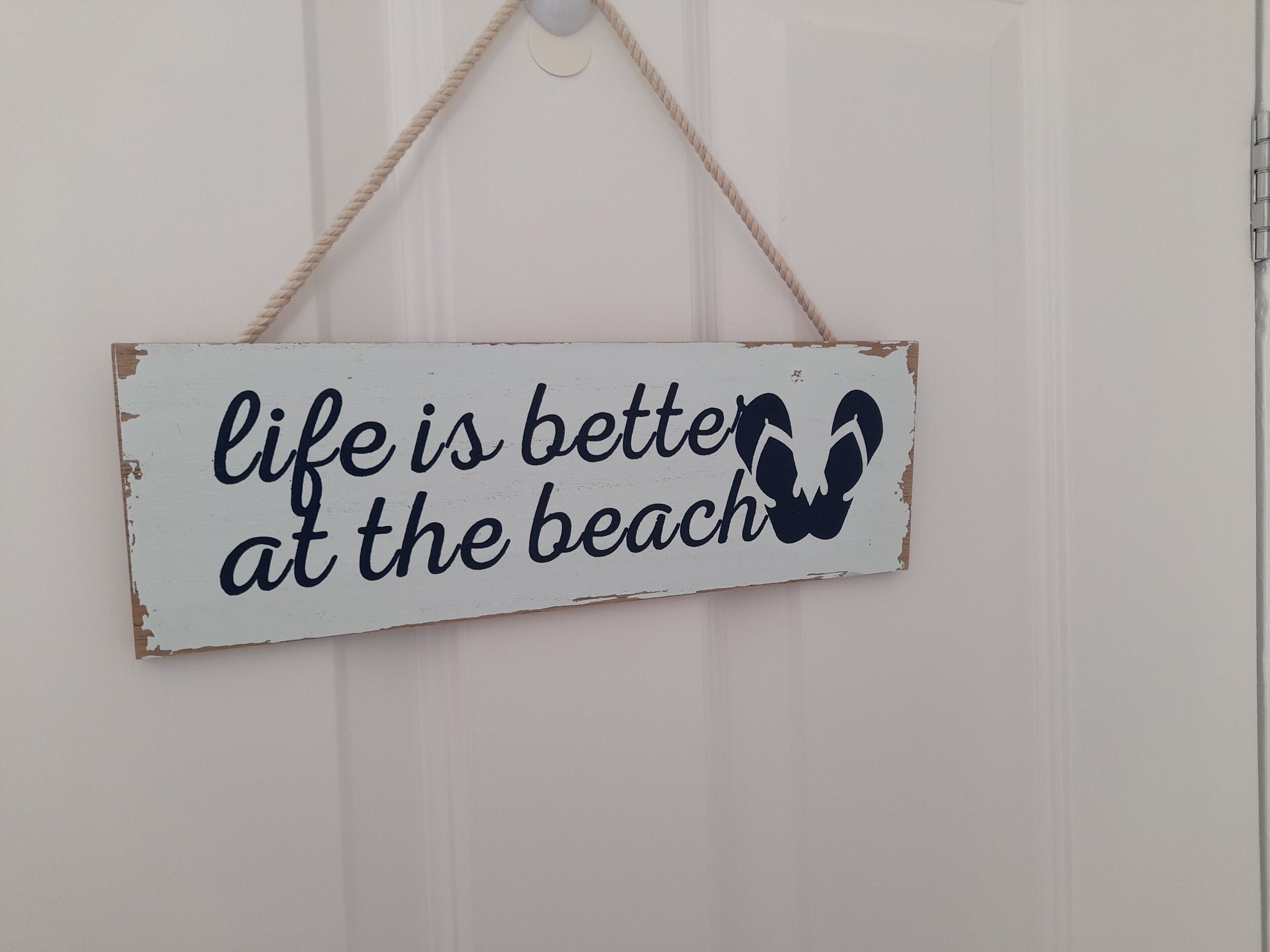 A sign with the text "life is better at the beach" and a silhouette of a person with a towel.