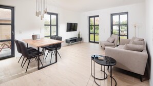 A spacious living area with a wooden dining table, black chairs, a beige sofa, and a black coffee table.