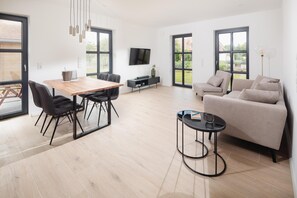 A spacious living area with a wooden dining table, black chairs, a beige sofa, and a black coffee table.