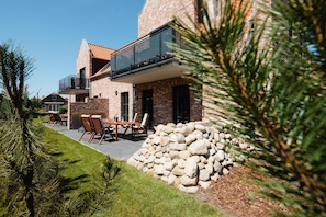 A modern house with a stone exterior, a balcony, and a patio with outdoor furniture. - Suite North | Direct waterfront location (Greetsiel)