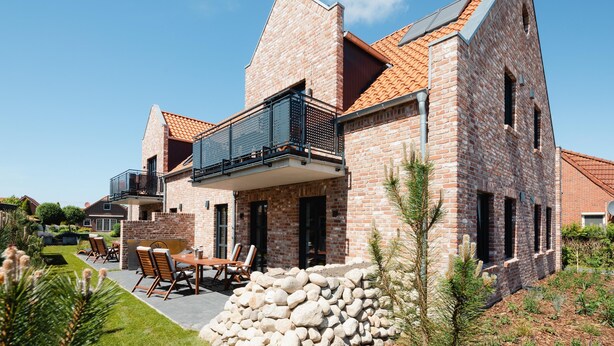 A modern brick house with a balcony, outdoor seating, and a stone wall.