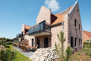 A modern brick house with a balcony, outdoor seating, and a stone wall.