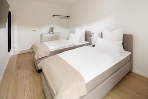 A bedroom with two beds, a bedside table, a lamp, and a door. - Suite North | Direct waterfront location (Greetsiel)