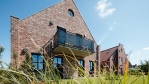 A modern brick building with a balcony, large windows, and a clear sky.