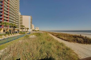 Ein Hotel direkt am Strand mit mehreren Etagen, einem Sandweg zum Strand und einer Reihe von Liegestühlen.