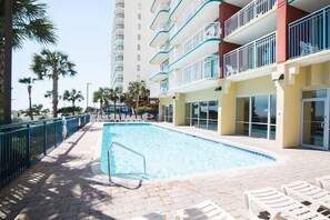 A swimming pool with lounge chairs, a blue fence, and a building with balconies. - Oceanfront Myrtle Beach Condo: Beach Views & Pool! (Myrtle Beach)