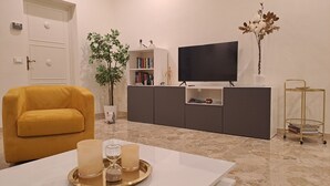 Ein Wohnzimmer mit einer Couch, einem Fernseher, einem Bücherregal, einer Pflanze und einem Tablett mit Kerzen.