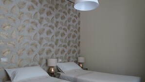 Ein Hotelzimmer mit zwei Einzelbetten, einem gemusterten Wandteppich, einer weißen Deckenleuchte und Nachttischlampen.
