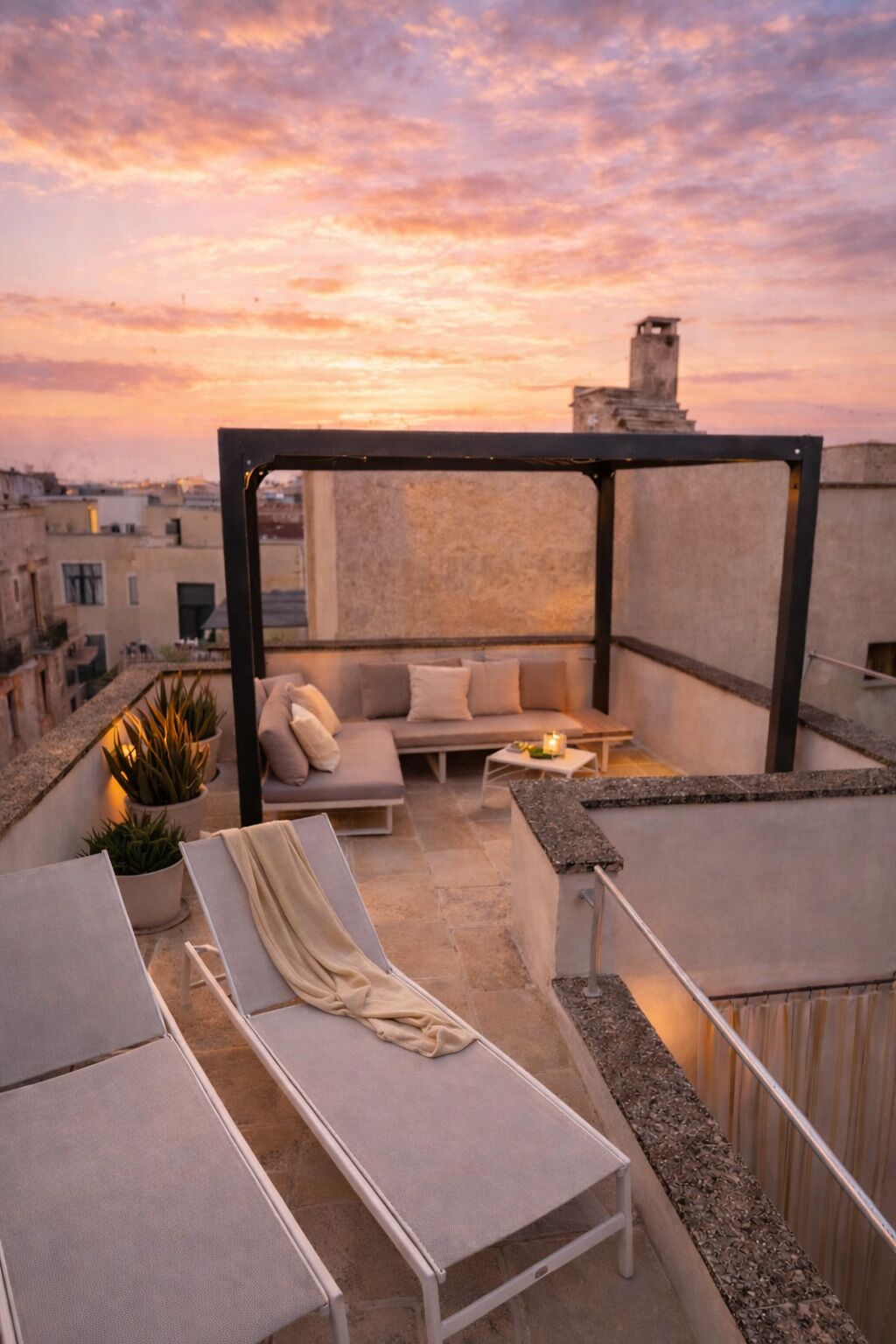 Une terrasse sur le toit, aménagée avec des chaises longues, un canapé et une petite table, le tout offrant une vue sur un magnifique coucher de soleil.