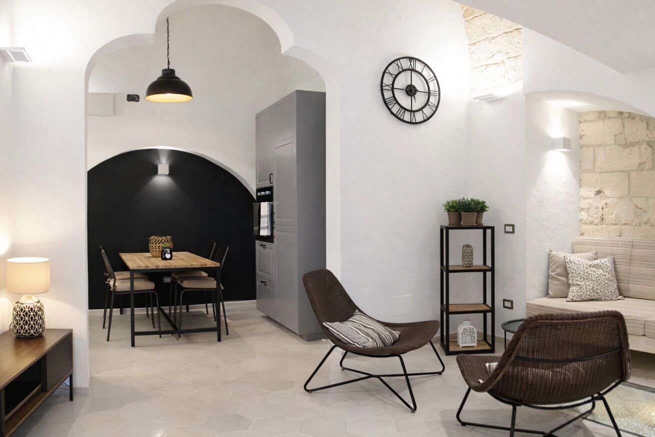 Ein modernes Interieur mit Essbereich, zwei Stühlen, einer Couch, einer Uhr und einem Bücherregal.