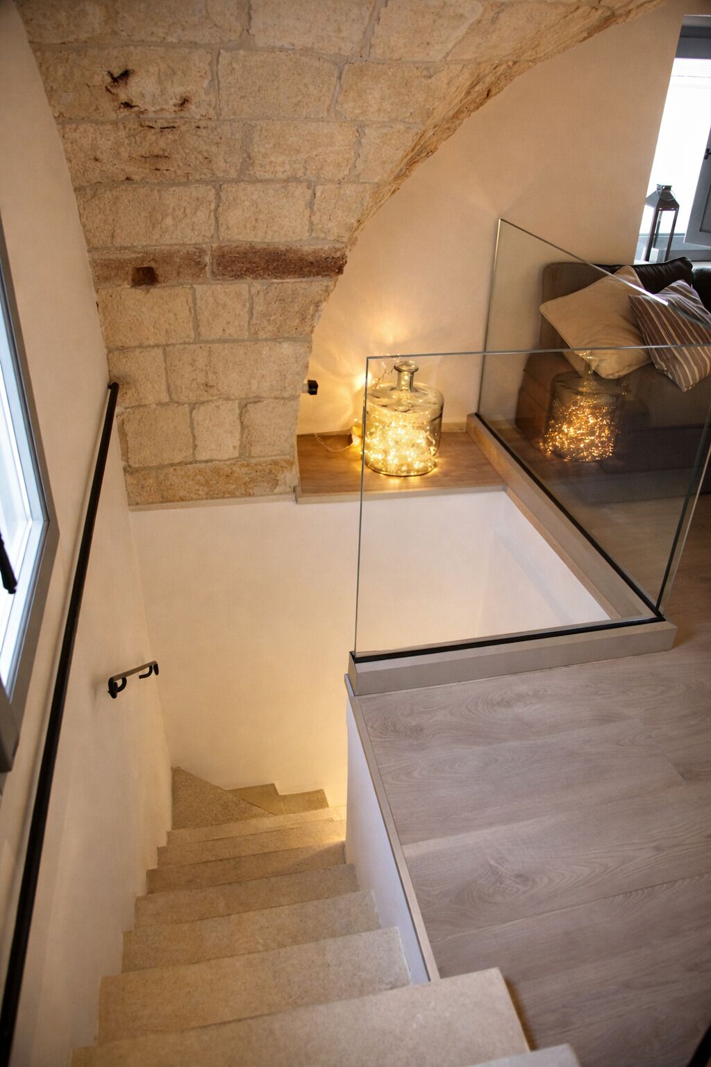 Eine Treppe mit einer Steinwand, einem Glasgeländer und einer Lampe.