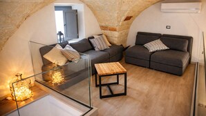 A cozy living area with stone arches, two grey sofas with patterned cushions, a glass coffee table, and a wooden side table.