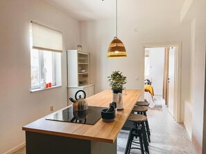 Eine moderne Küche mit einer Holztheke, einer hängenden Pendelleuchte, einem Topf mit Pflanze und Blick in den Essbereich.