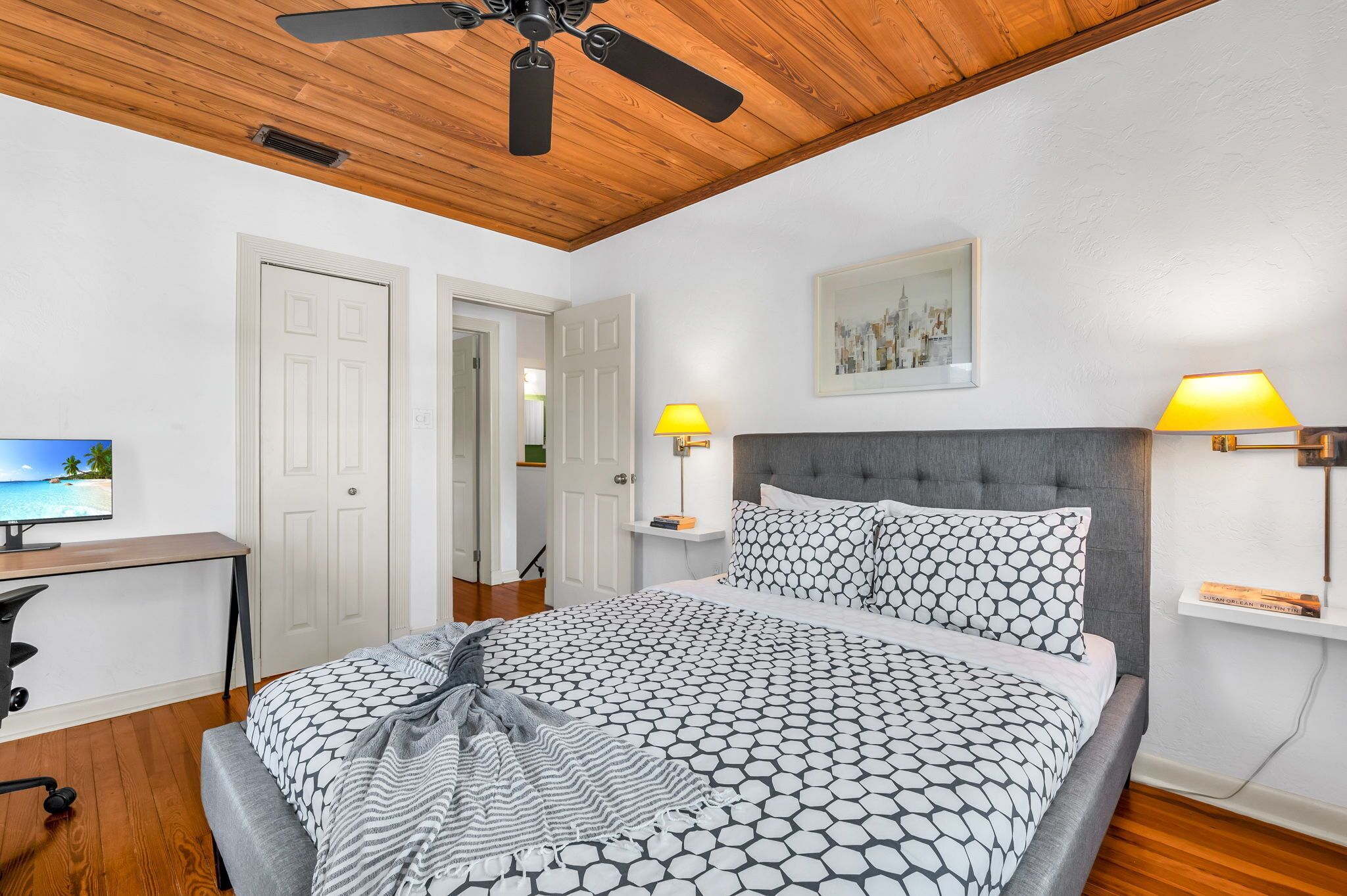 Un dormitorio con cama, escritorio, computadora y ventilador de techo.