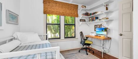 Un dormitorio con cama, escritorio con computadora, silla, ventana con persianas y ventilador de techo.