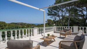 Ein Balkon mit Korbmöbeln, einem weißen Geländer und Blick aufs Meer.