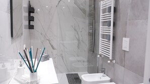 Un baño moderno con tocador de mármol, dos inodoros, ducha y zona de ducha con mampara de vidrio.