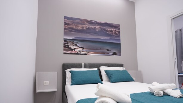 Un cuarto de hotel con una cama, vista al mar y un cuadro de una escena costera.