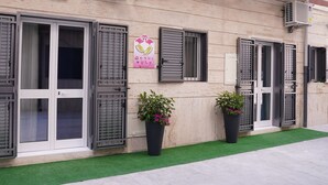 Un edificio con varias ventanas, algunas con contraventanas, y un cartel que indica que es un negocio.