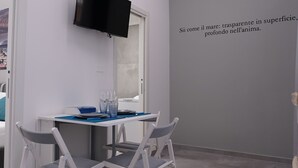 Una habitación moderna con televisor de pantalla plana montado en la pared, una mesa con sillas y una pared decorada con una cita en italiano.