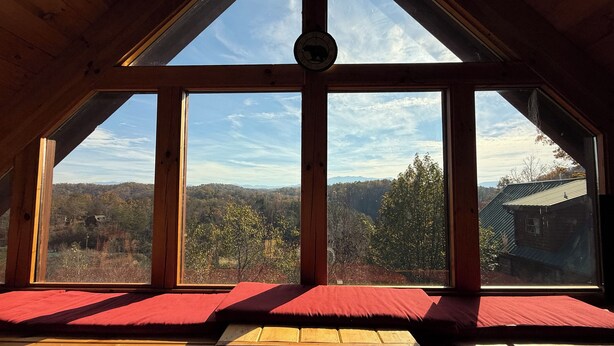 Ein Zimmer mit einem großen Dachfenster und Blick auf eine bewaldete Bergkette.