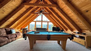 Ein Dachzimmer mit Billardtisch, einer Couch und einem Fernseher.