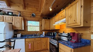 Eine Holzhütte mit einer Küchenzeile, inklusive Backofen, Kaffeemaschine und einem Fenster mit Blick auf Bäume.