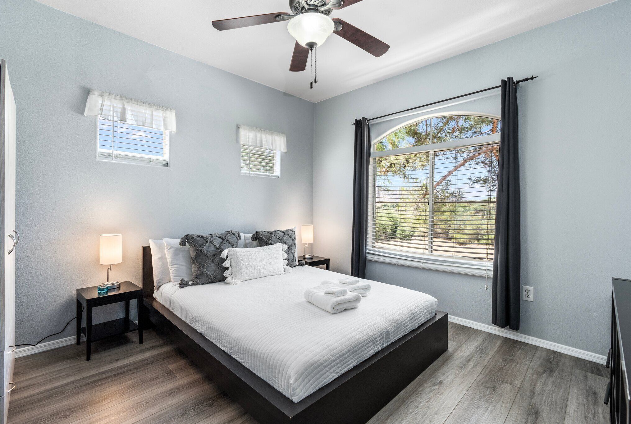 A bedroom with a bed, nightstands, a ceiling fan, and a large window with curtains.