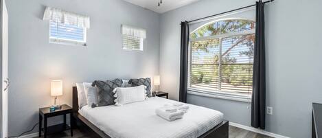 A bedroom with a bed, nightstands, a ceiling fan, and a large window with curtains.