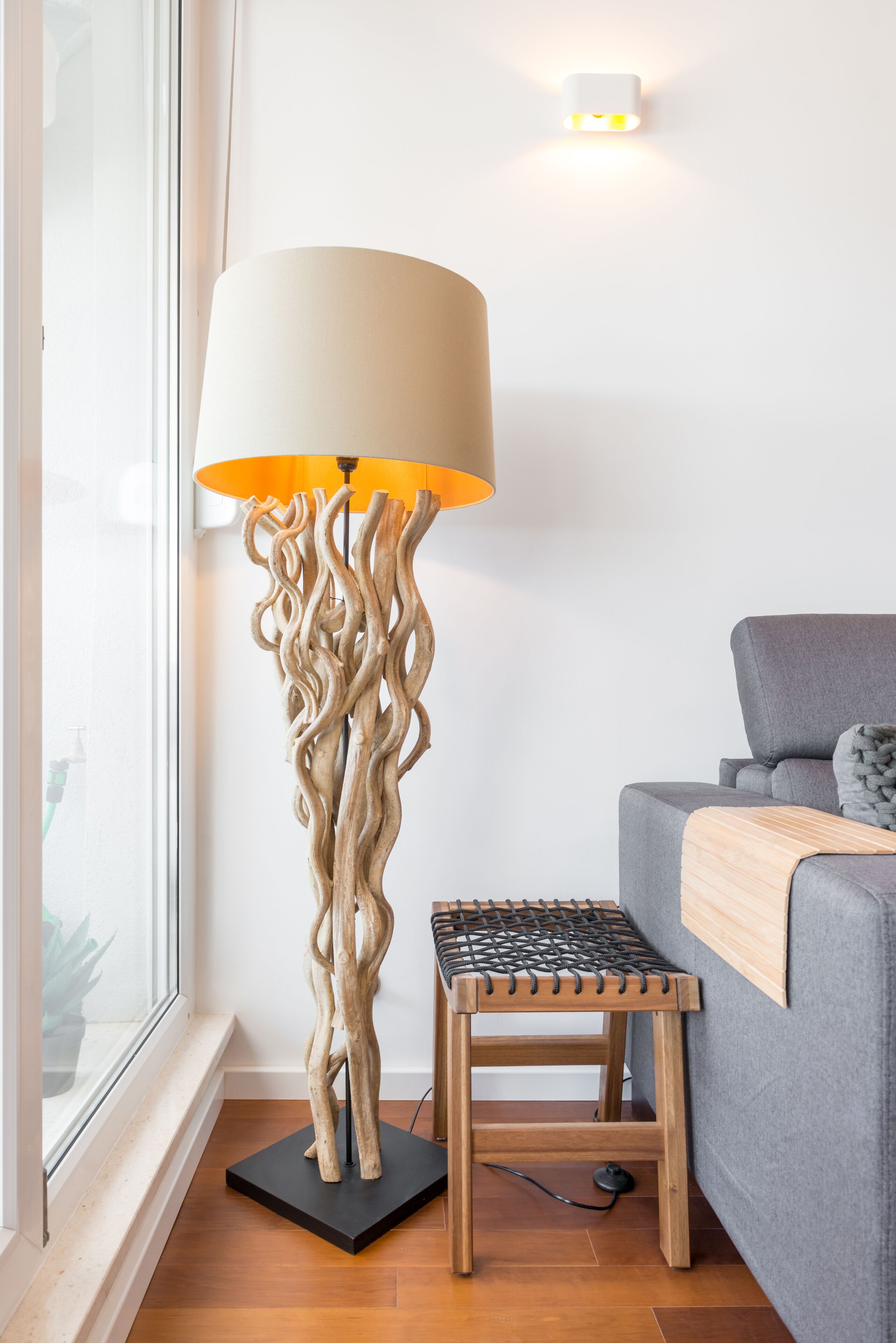 A modern room with a unique floor lamp, a small wooden stool, and a grey sofa.