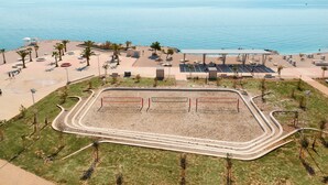 An aerial view of a beachside area with a sandy beach, palm trees, and a fenced sports court. - Sun Spalato Beach & Palms (Split)