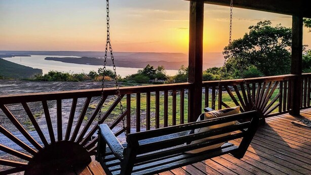 Un terrazzo in legno con una sedia a dondolo e vista su un tramonto sull'acqua.