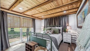 Una camera da letto con un letto, comodini, una finestra con tende, un soffitto in legno e vista sull'esterno.