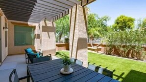 Un patio cubierto con mesa y sillas, un jardín pequeño y vistas del entorno verde.