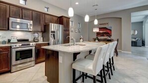Una cocina moderna con armarios de madera oscura, electrodomésticos de acero inoxidable, una isla grande con taburetes de bar e iluminación colgante.
