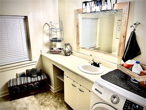 A bathroom with a sink, mirror, and washing machine. There is a towel rack and a basket on the counter. - River Rock Cabin - Private Escape - ON the Etowah River! Private decks/firepits! (Dahlonega)