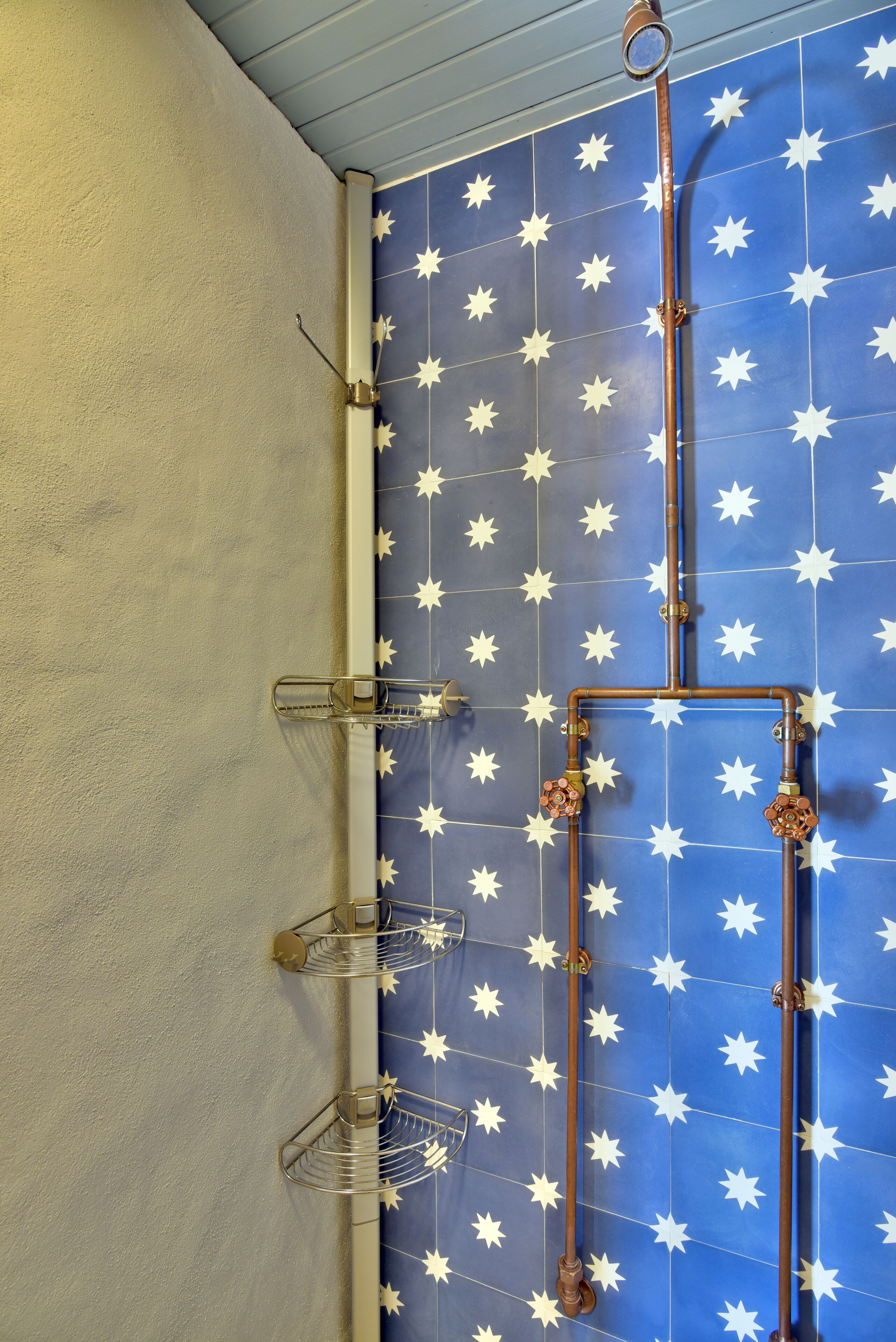 A bathroom with a blue star-patterned wall, a white door, and a copper shower system.