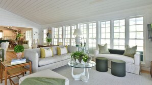 A spacious living room with a large window, a sofa, a glass coffee table, and a dining area in the background. - Lake Life Retreat 3BR Home w/ 2 Kitchens & Docks (Warwick)